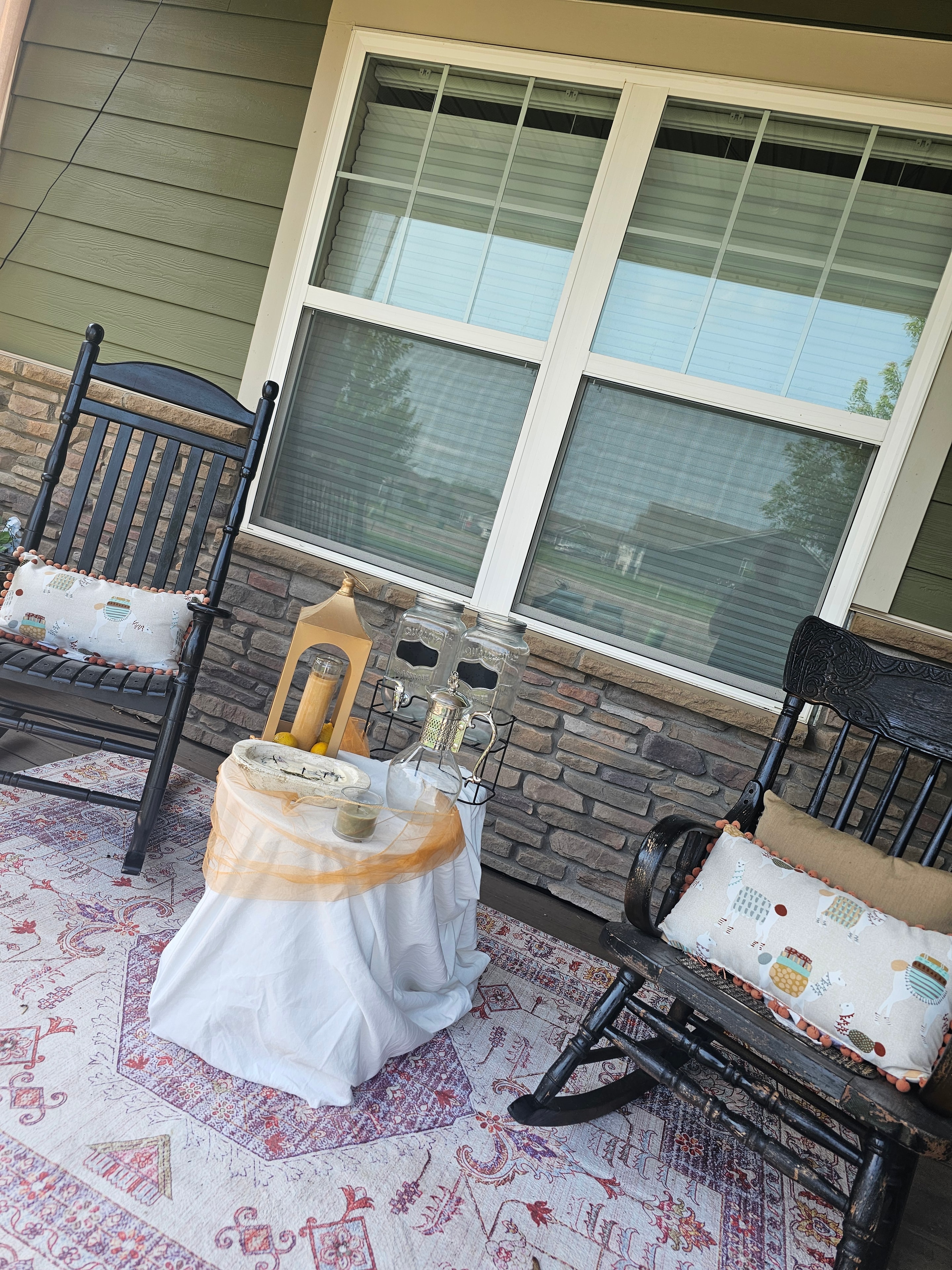 Front porch seating area with black iron chairs, patterned cushions, and lanterns